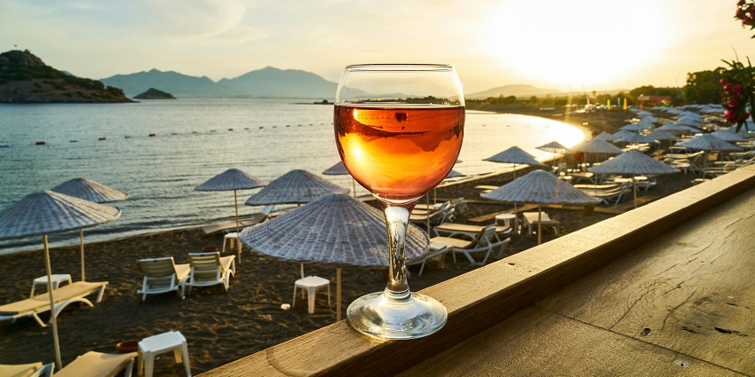 A glass of wine on a ledge with sunset and beach shacks in the background.