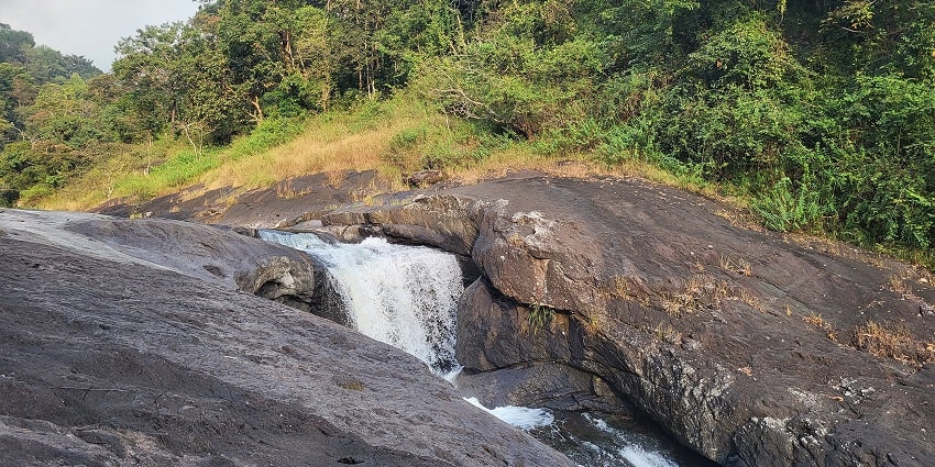 View of streams flowing over smooth rocks into a clear and small pool in Kerala