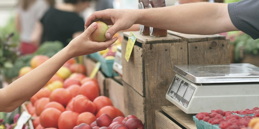 A fruit and vegetable seller handing over a fruit to the customer in a crowded market.