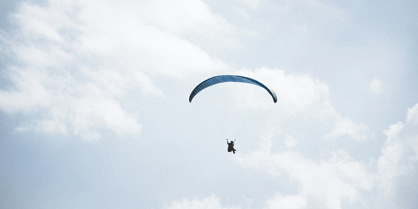 A stunning landscape of a person paragliding during the daytime under soft clouds.