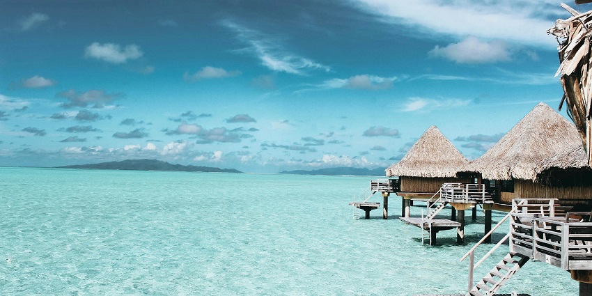 A front view of two cottages in the middle of the sea with crystal clear water.