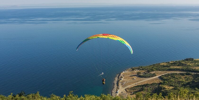 A view of a person paragliding with a colourful parachute flying over a body of water.