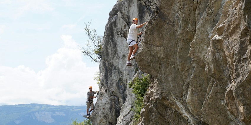 Two men clicked while rock climbing with a scenic backdrop of cloudy skies and mountains