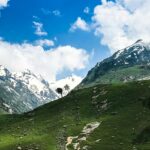 A breathtaking view of lush green grass near snow-covered mountains under dense clouds.