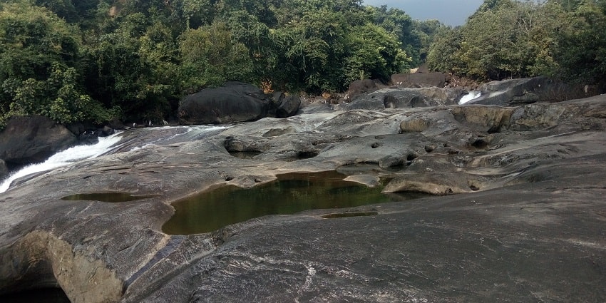 Waterfall surrounded by scenic forested hills and rocky terrain - Kozhikode Waterfalls
