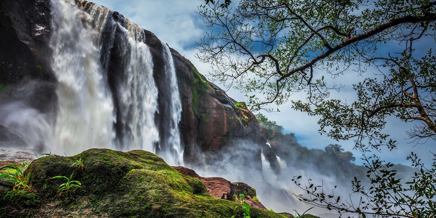 Image of Athirapally waterfalls surrounded by lush greenery under clear blue sky view