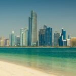 A view of the skyline of UAE with a turquoise body of water in front during the daytime.