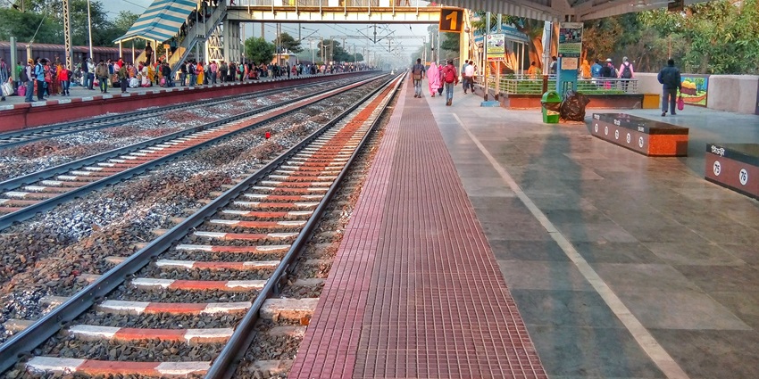 Image of railway track leading to a station, with trains and platform bustling with activity.
