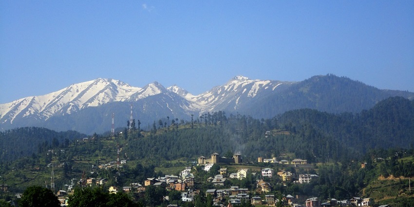An image of Bhaderwah, a lush valley surrounded by forested hills under a clear blue sky.