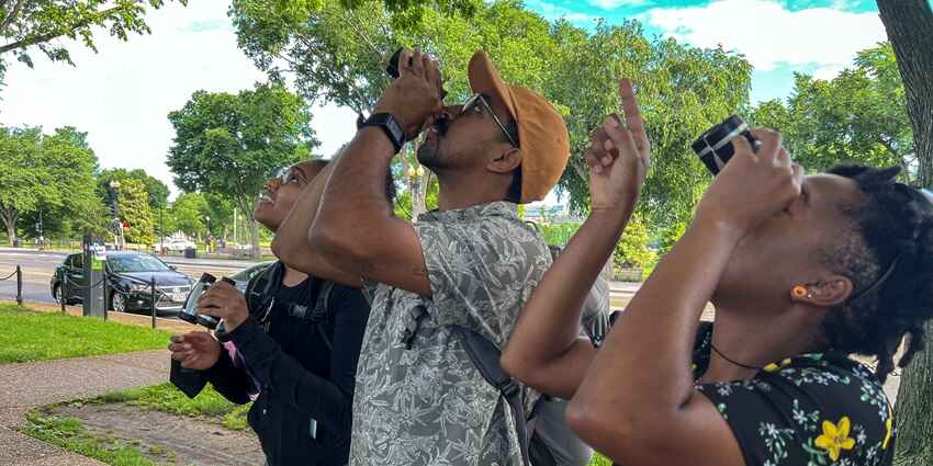A group of three tourists clicked while looking up & trying to spot birds via binoculars