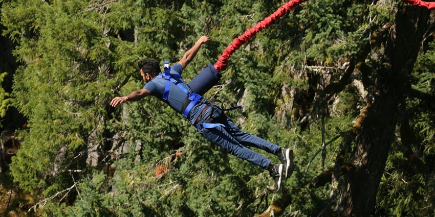 An aerial view of a harnessed man jumping off a lush green cliff during Bungee jumping.