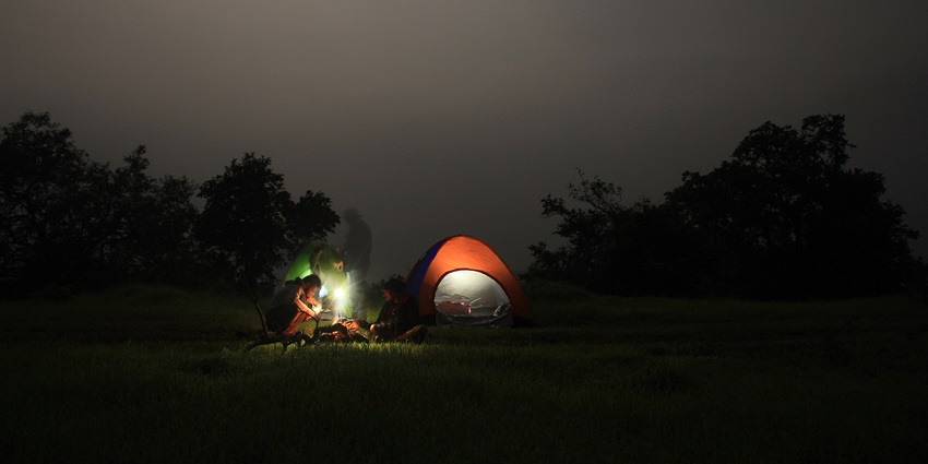 Camping under a starlit sky in Tamhini Ghat, with glowing tents pitched on a grassy clearing.