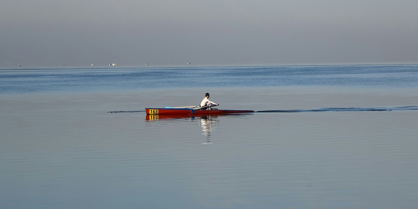 A distant view of a red canoe on a body of water with a man rowing it during the daytime.