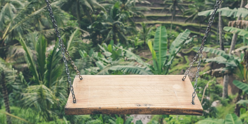 A stunning view of a green forest with a brown wooden swing attached with grey chains.
