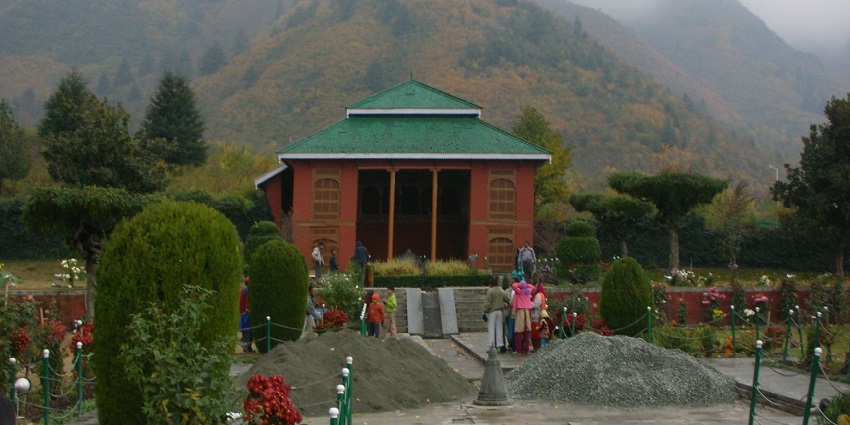 Chashme Shahi with, vibrant flowerbeds, and a pavilion, set against a mountainous backdrop