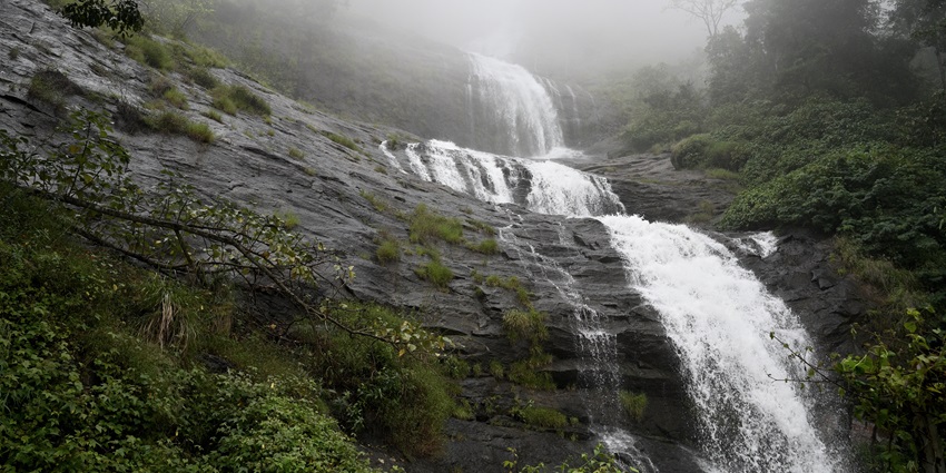 A picture of a majestic waterfall in Kerala with a strong stream falling onto a rocky pond