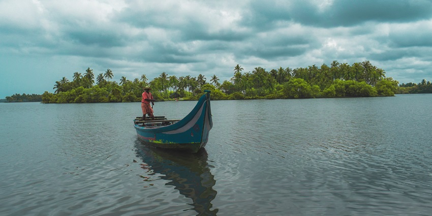 A mindblowing view of the backwaters of Kerala with a boat on it encircled by green trees.