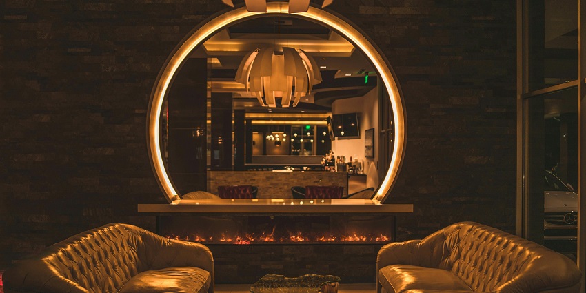 Lounge with leather sofas, a circular mirror, and ambient lighting above a warm fireplace.