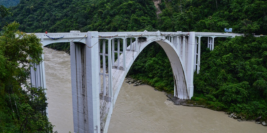 A picture of a stunning bridge connecting two landmasses surrounded by greenery and cliffs