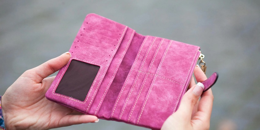 A woman holding a pink suede wallet in her hands.