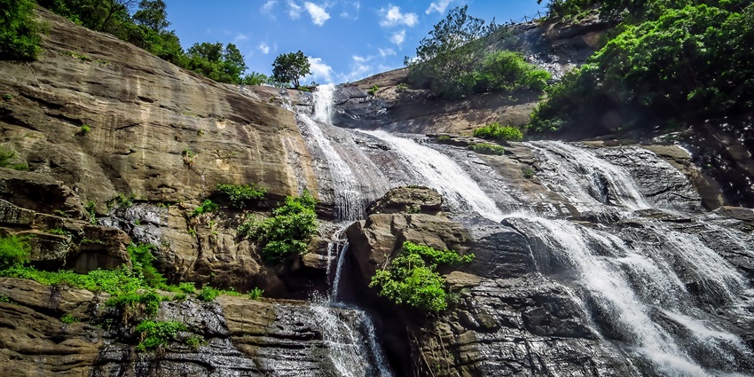Scenic view of cascading water streams at Courtallam Five Falls, surrounded by rocks.