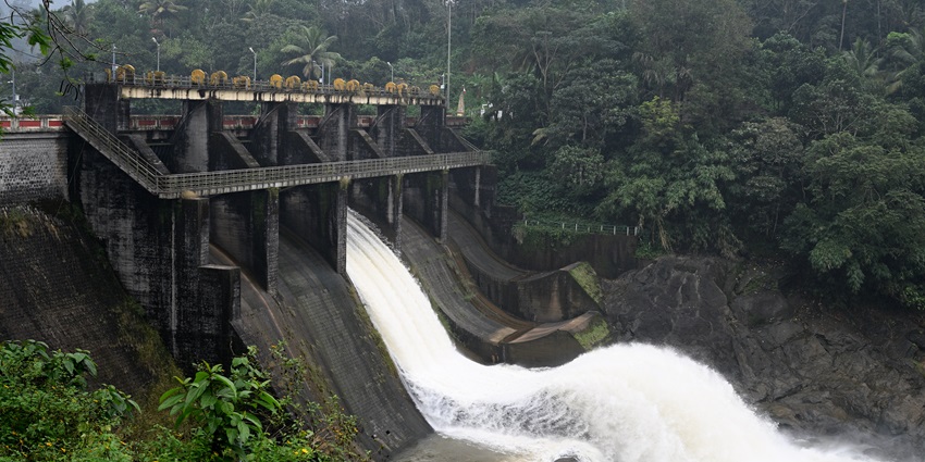 A dam with an open spillway releasing water into a lush green landscape.