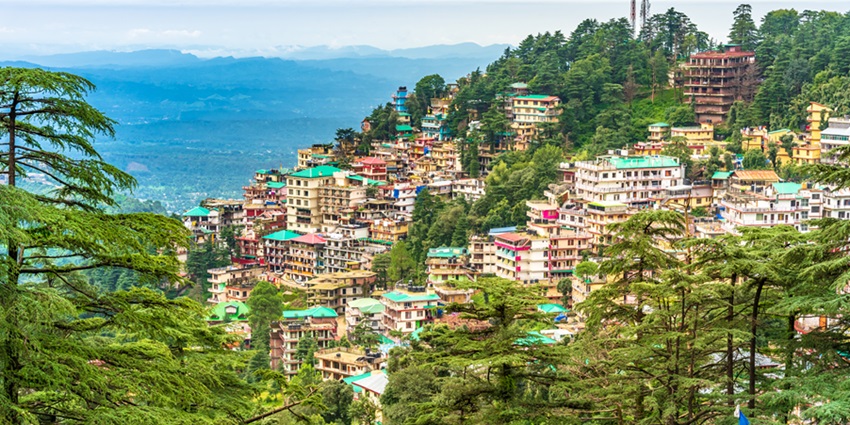 A distant shot of Dharamshala tucked amidst the snow-capped mountains and green forests