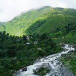 A stunning green view of a valley in Dharamshala with a stream of water flowing through.