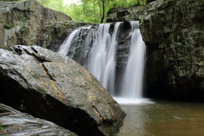 An enchanting view of majestic waterfalls surrounded by lush green tall trees and rocks.