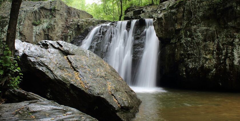 An enchanting view of majestic waterfalls surrounded by lush green tall trees and rocks.