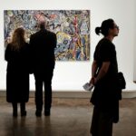 A view of a group of people admiring paintings and clicking pictures in a museum