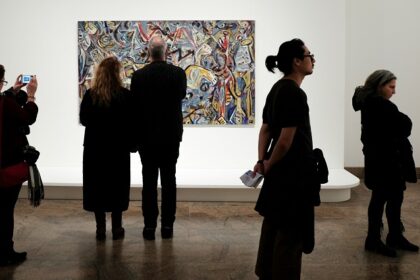 A view of a group of people admiring paintings and clicking pictures in a museum