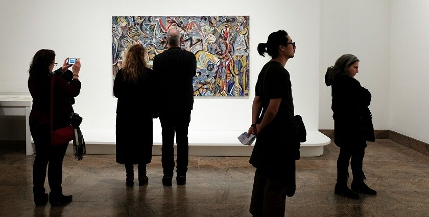 A view of a group of people admiring paintings and clicking pictures in a museum