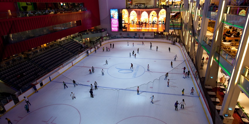 People enjoying ice skating at the Dubai ice rink with seating and advertisements around.