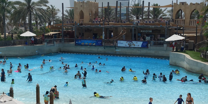 People enjoying the wave pool at a water park with a scenic backdrop of palm trees.