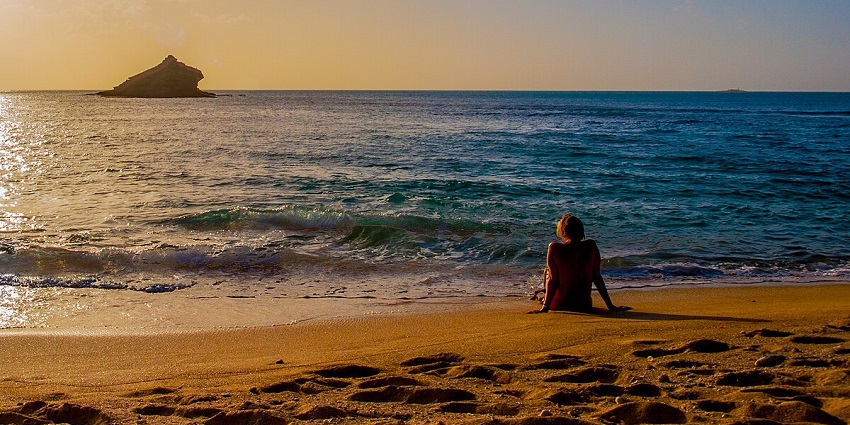 View of women sitting on a beach and looking at mesmerising sunset hues in the sky