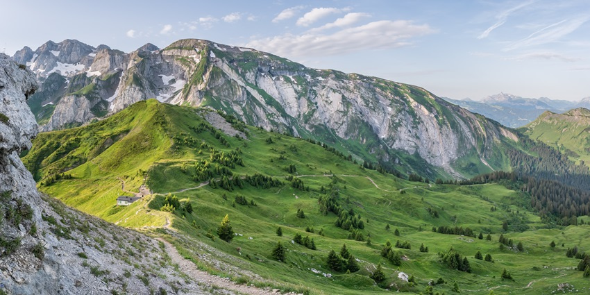 A picture of a scenic hill station in France with a lush green valley in front of the barren hills