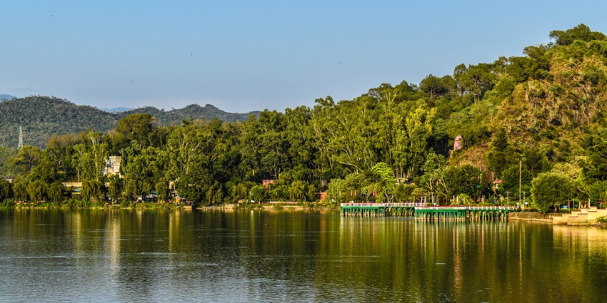 serene view of a glistening lake that is shaded by trees and hills in the backdrop