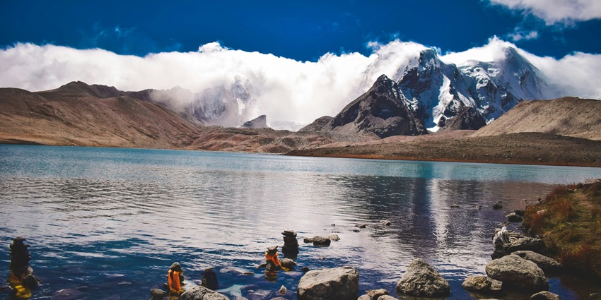 A scenic view of the dazzling waters of the Gurudongmar Lake in front of misty peaks.