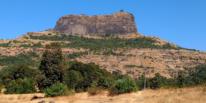 A picture of the ruins of a historical fort perched on top of a lush mountain in Nashik