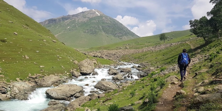 Trekkers with horses by Tarsar Lake, surrounded by lush hills in Jammu and Kashmir.