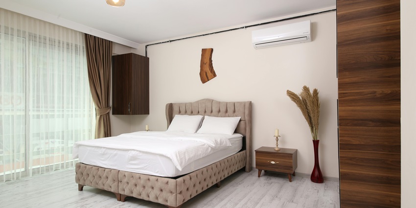 A simple hotel room. There is a bed, a table, curtains and a side table inside the room.