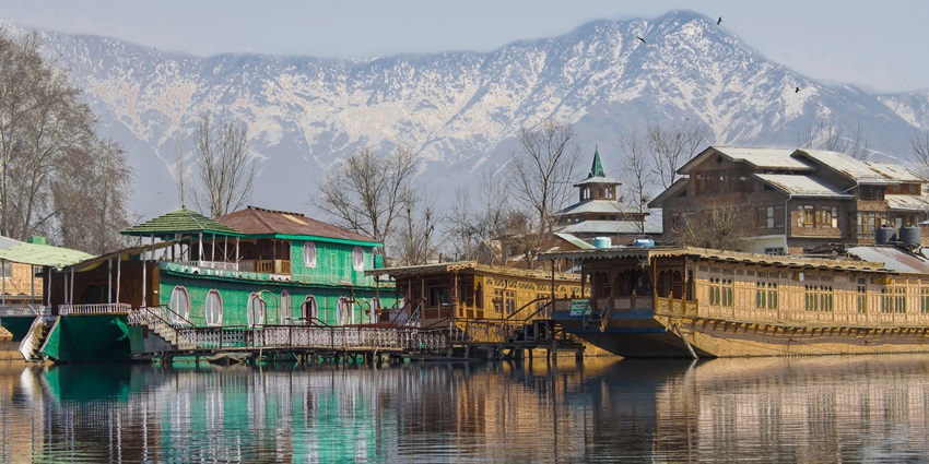 Green and brown wooden houses on the Dal Lake with the backdrop of the snow-covered mountains