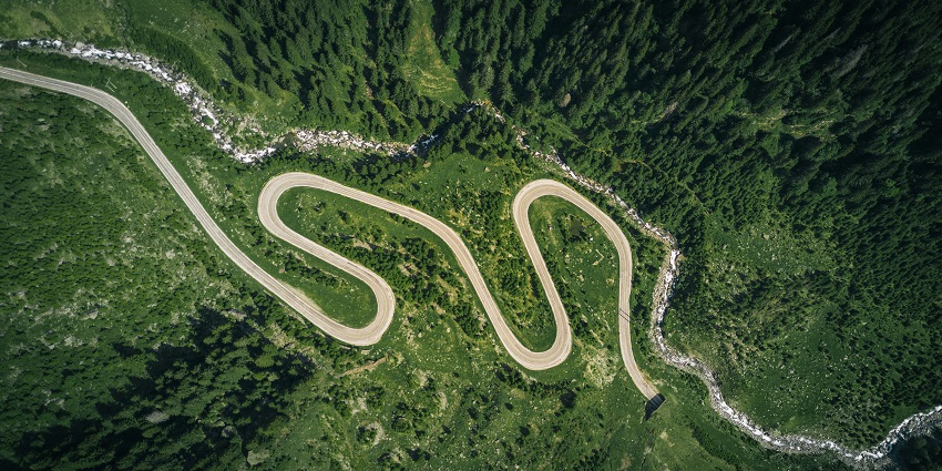 An aerial view of a long strip of road encircled by lush green hills during the daytime.