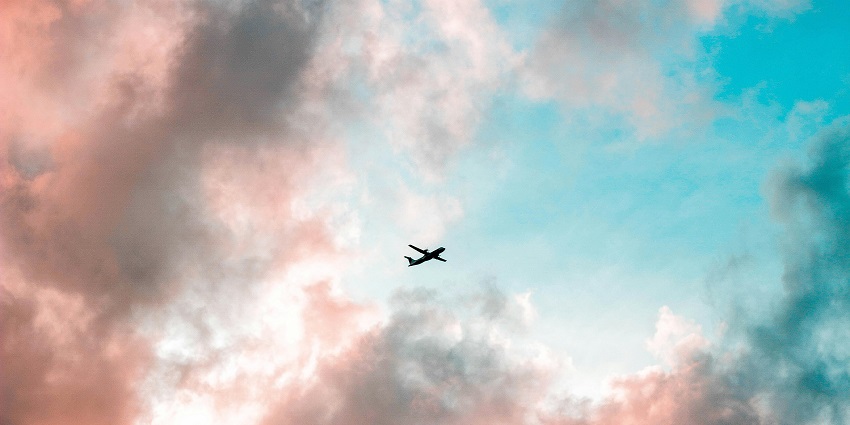 A view of an aeroplane flying amidst dense clouds in a colourful sky during the daytime.