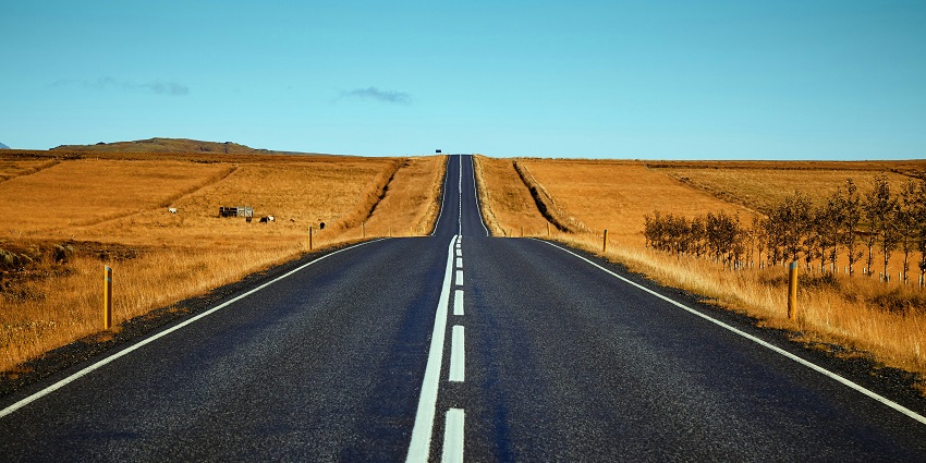 A day view of a straight road leading up to a hill with golden sands on both sides.