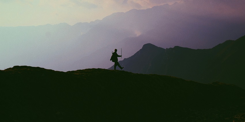 A mesmerising silhouette of a man trekking up the hill with a stick in his hands.