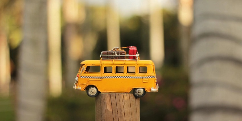A front view of a yellow miniature bus on a wooden pole with luggage on top of it.