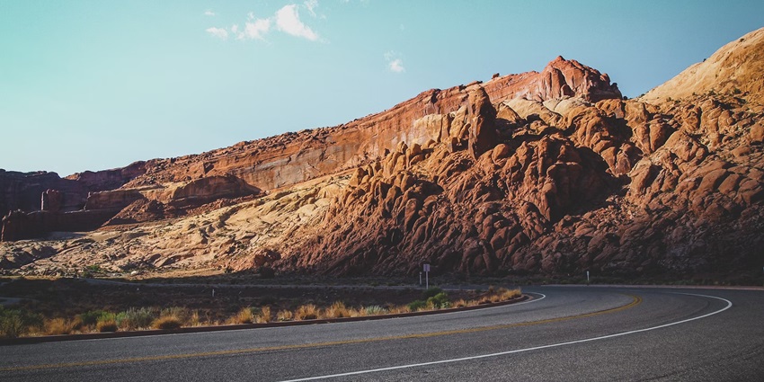 A view of a long road between rocky mountains during the day time under soft clouds.
