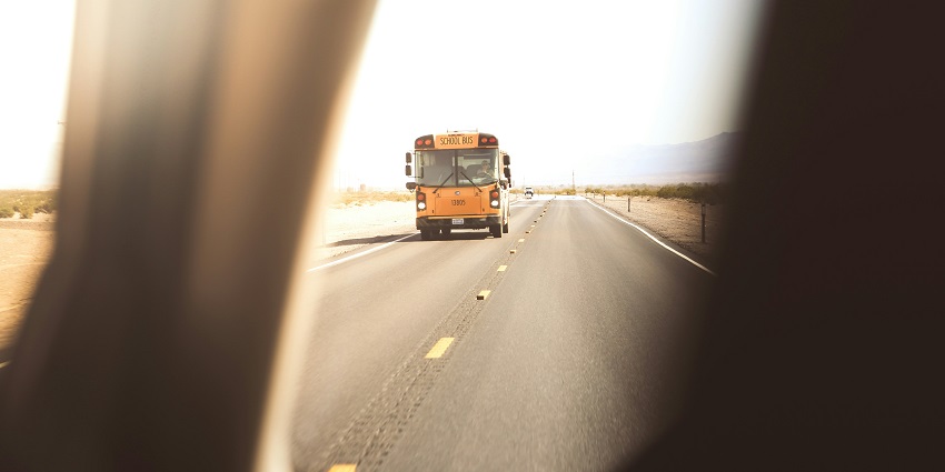 A view of a yellow bus on a wide road with mountains at a distance in the background.
